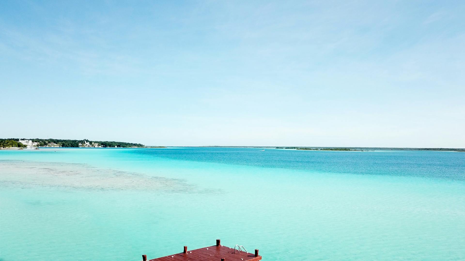 Beautiful turquoise waters of Bacalar Lake in Mexico with a wooden dock and clear blue sky.