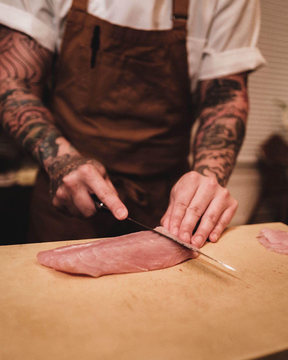 What is a slicing knife used for: clean single-stroke cuts Chef slicing raw meat with a long slicing knife on a wooden cutting board