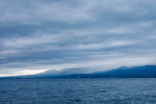 Scenic ocean expanse with mountain backdrop under a cloudy sky, capturing nature's tranquility.