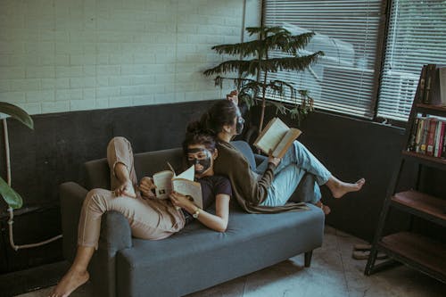 Two Women Leaning on Each Other's Back While Reading a Book