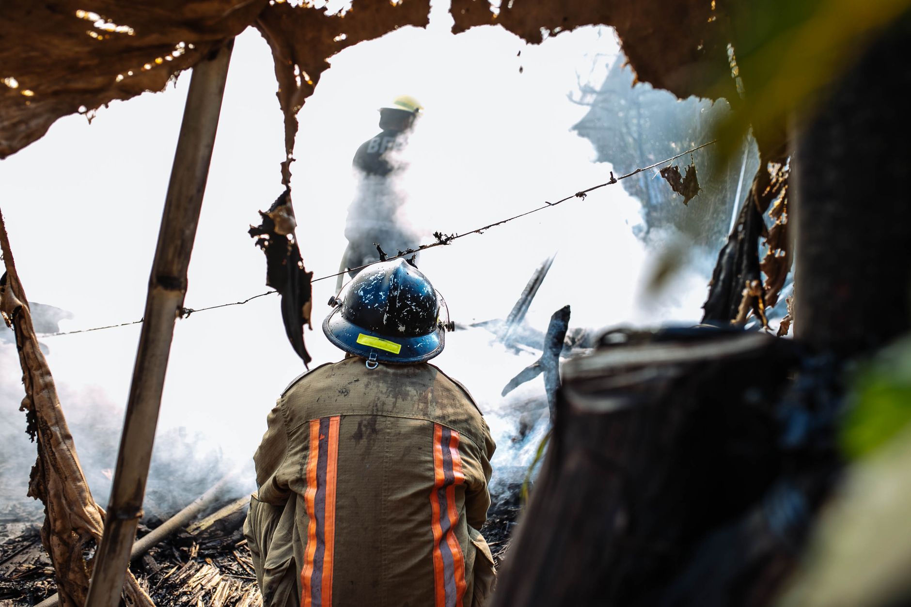 Firefighters in action, handling smoke and debris during daylight outdoors.