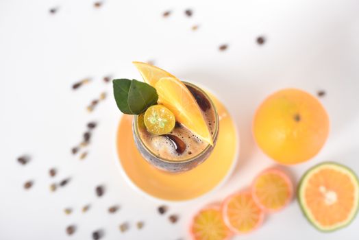 Top-down view of a citrus iced drink with orange slices and green leaves on a white background.
