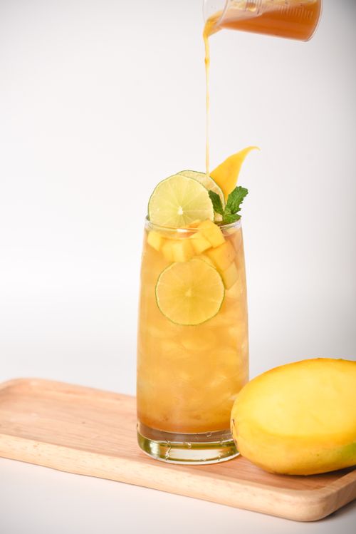 Free A tall glass of mango juice garnished with lime slices and mint on a wooden tray. Stock Photo