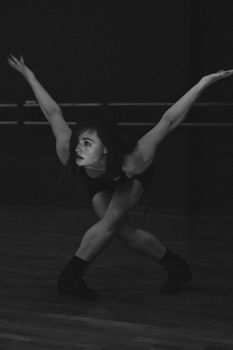 Graceful dancer captured mid-movement in a monochrome studio setting, highlighting flexibility.