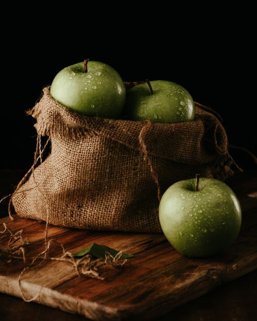 Free Still life of green apples with water droplets in a rustic burlap sack on wooden surface. Stock Photo