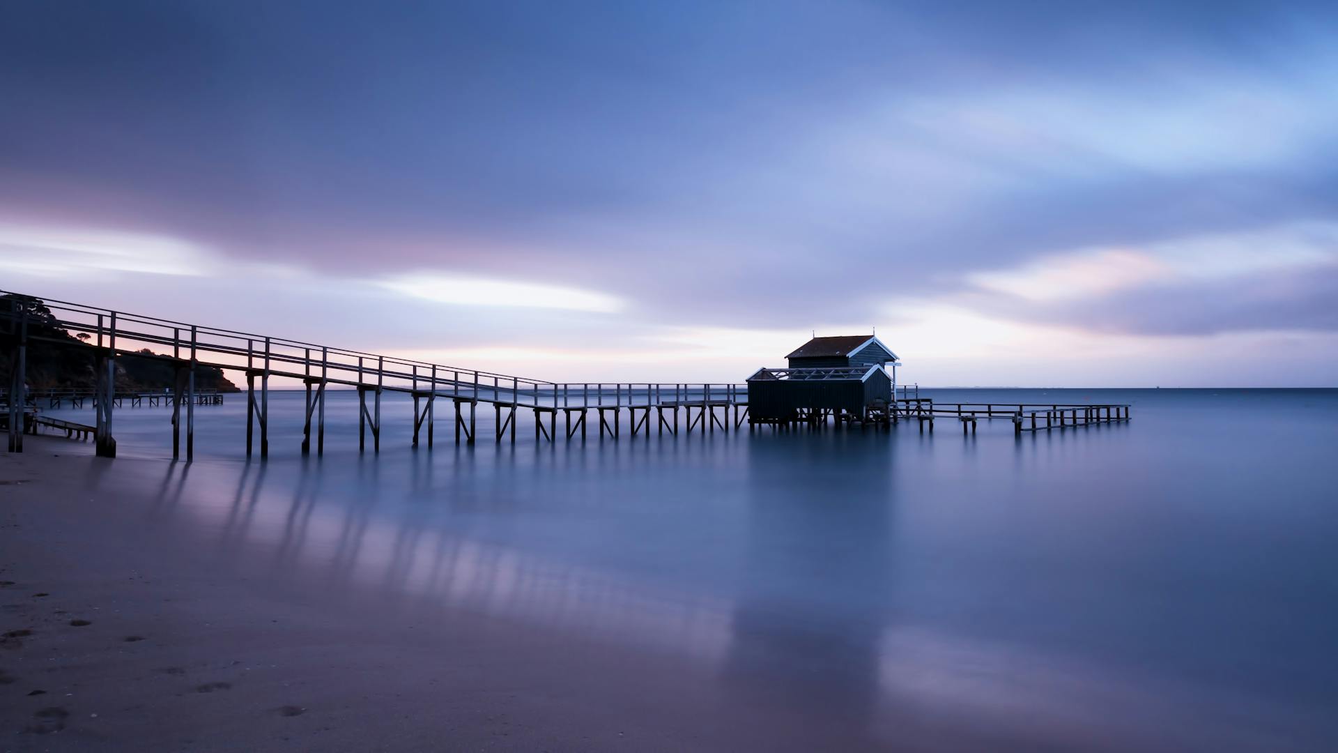 Peaceful scene of a beach pier extending into calm ocean waters at twilight, under a serene sky.