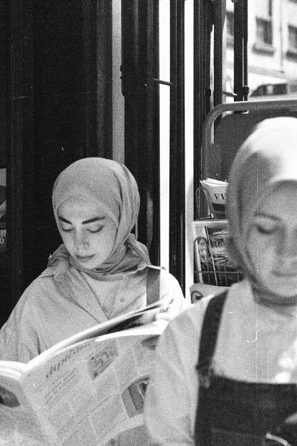 Black and white photo of young women wearing hijabs, reading newspapers outdoors.