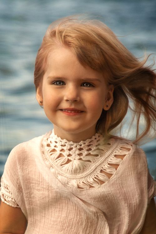 Free Portrait of a beautiful young girl smiling with windblown hair against a serene seaside background. Stock Photo