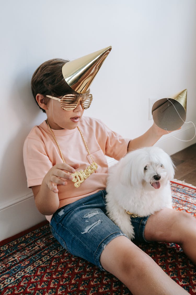 A Boy Wearing A Party Hat And A Dog Sitting On His Lap