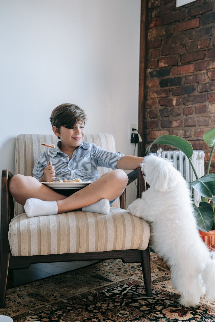 A Kid Reaching Out For His Dog While Eating