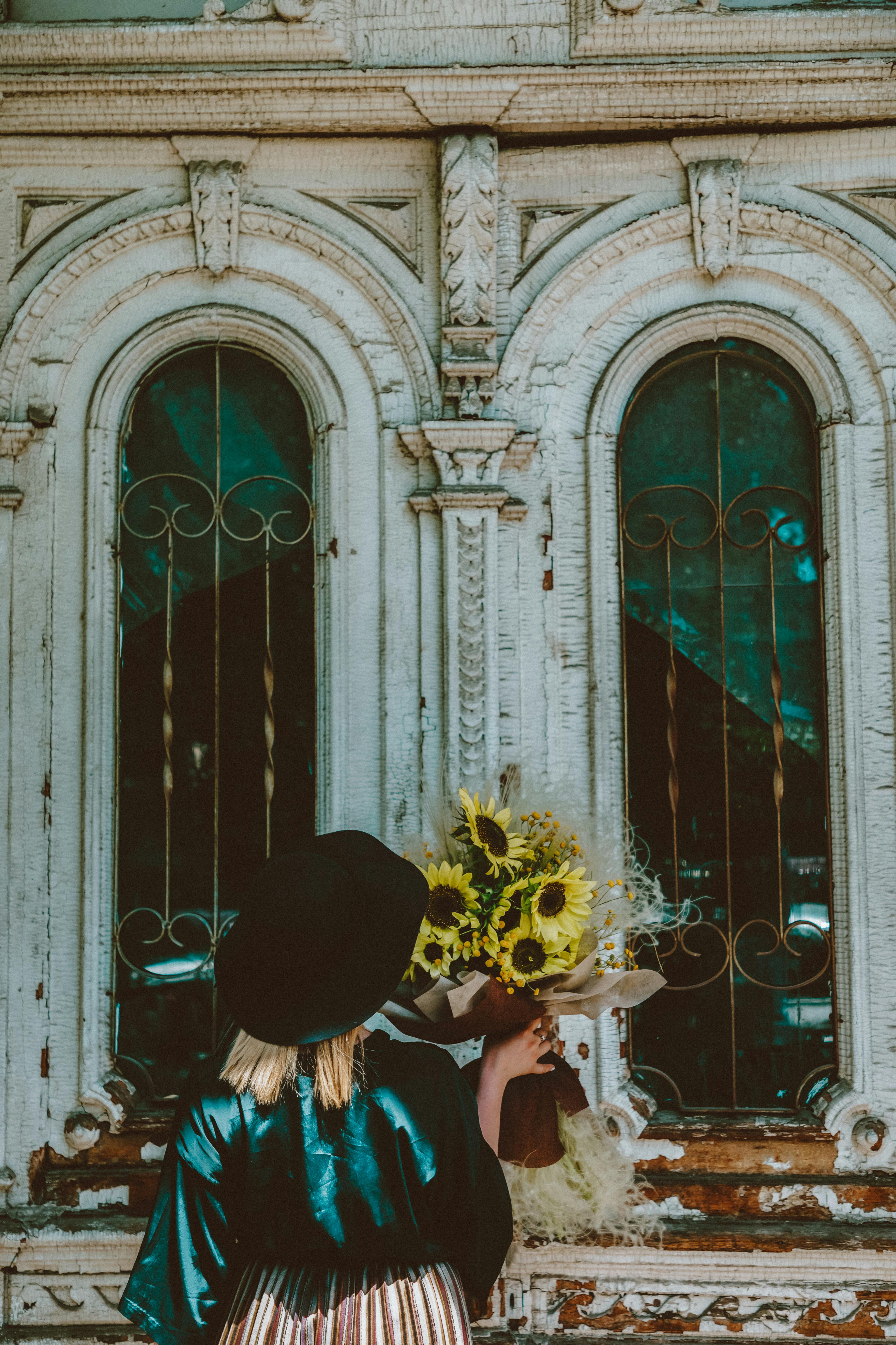 woman in black hat standing in front of glass window with flower bouquet