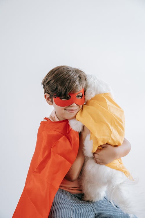 Boy with Red Eye Mask and Cape carrying a White Dog 