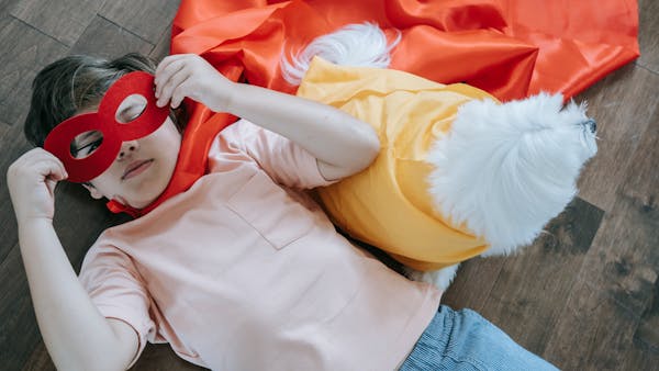 Boy in superhero costume with dog companion, lying on wood floor in playful pose.