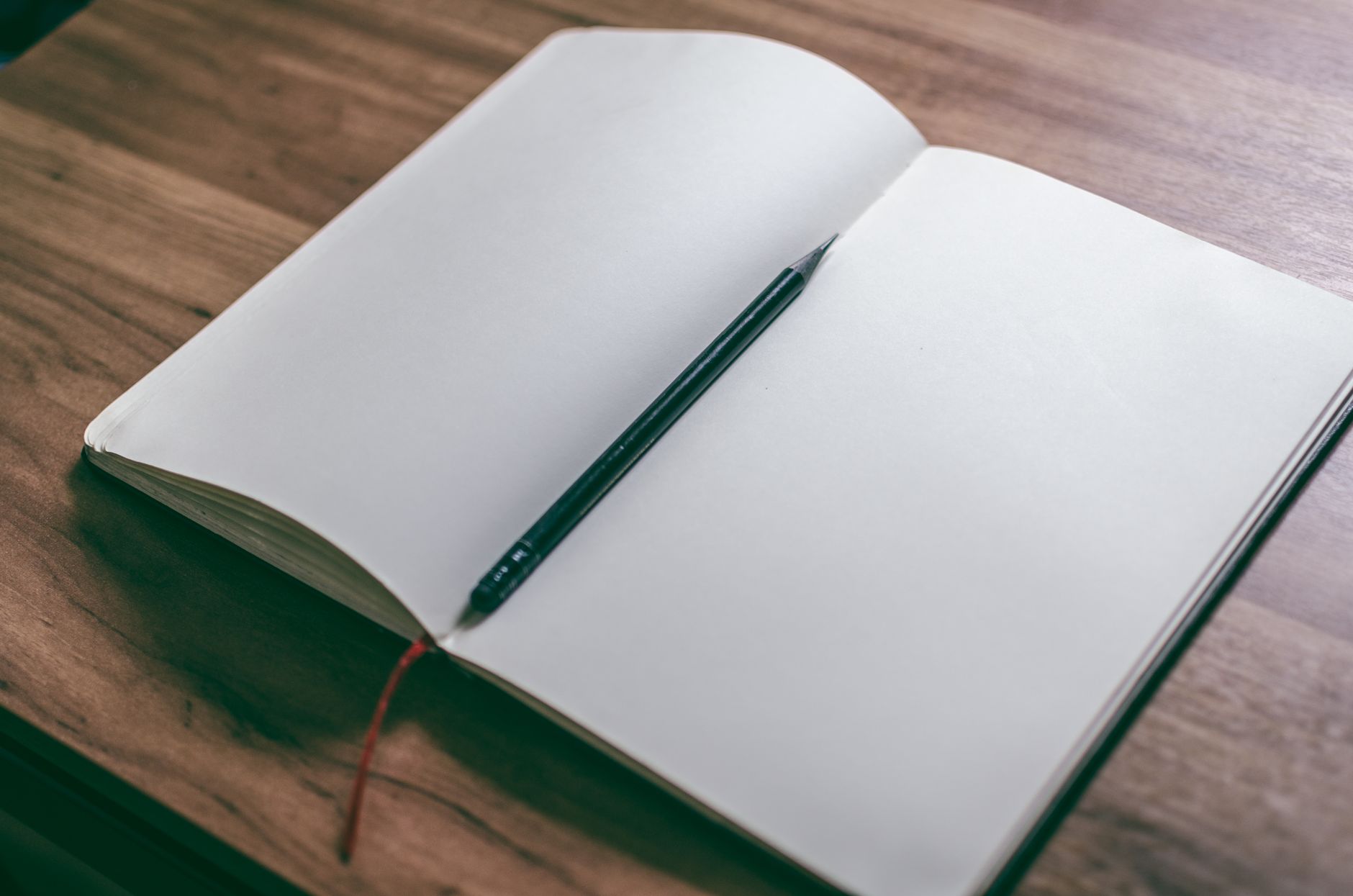 Open sketchbook and pencil on wooden desk, perfect for creativity and design concepts.