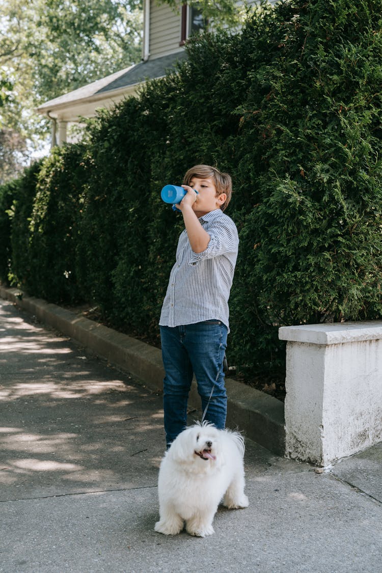 Boy Drinking Water And Standing With Dog