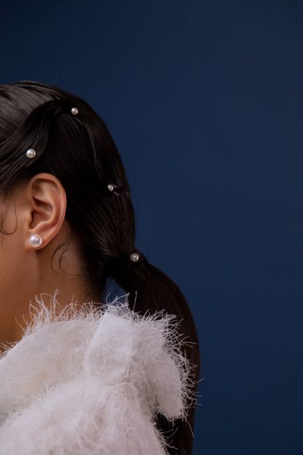 Fotomural Primer plano de una persona con perlas y un atuendo blanco texturizado frente a un fondo azul.