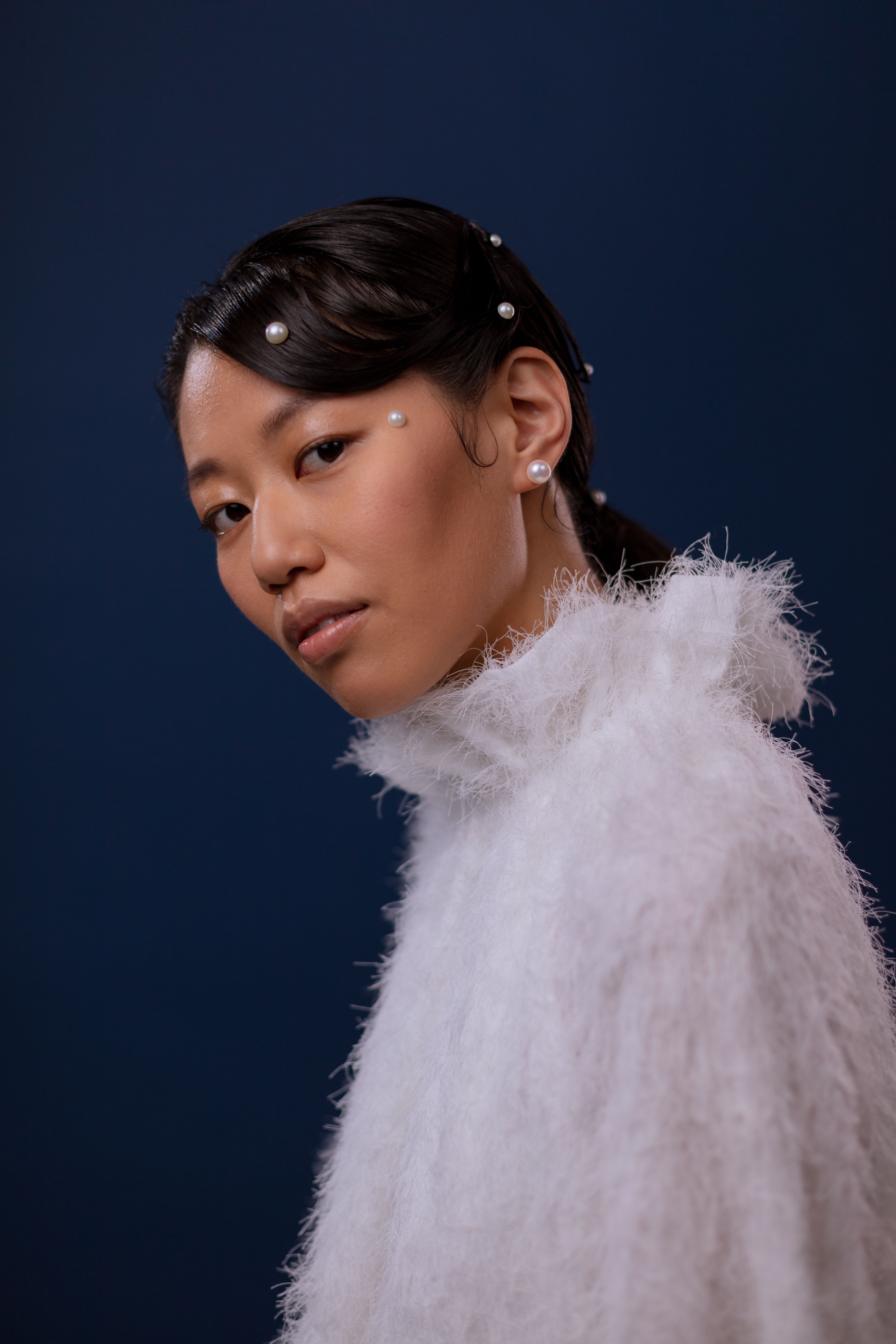 Portrait of an Asian woman with a pearl-adorned hairstyle against a blue background.