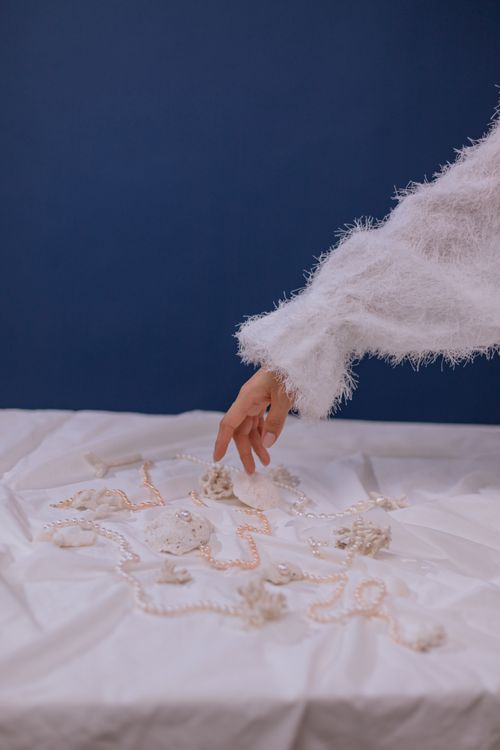 Free A delicate hand reaching for pearls on a white surface against a blue background, symbolizing elegance. Stock Photo