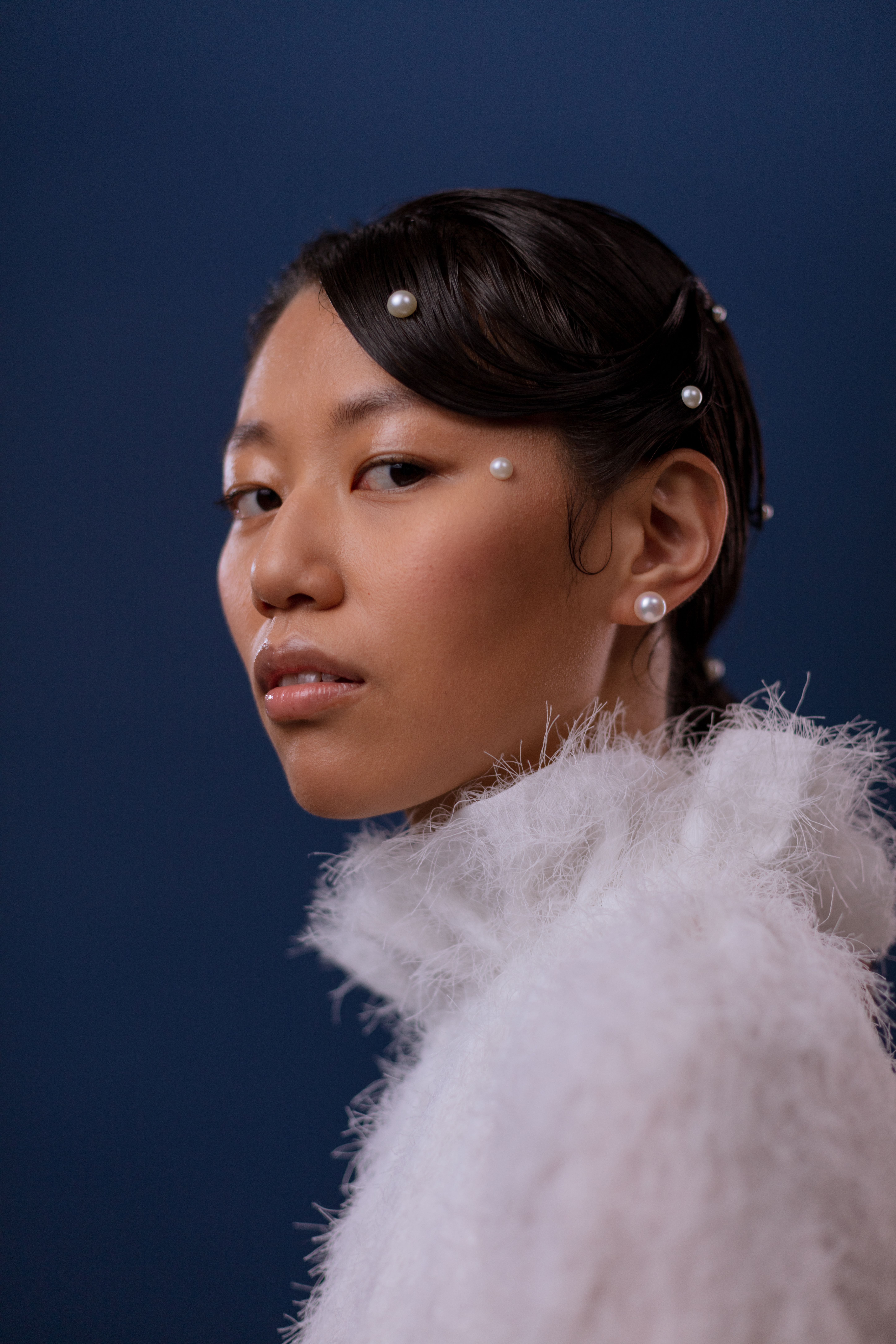 Elegant portrait of a woman adorned with pearls against a blue background, exuding beauty and class.