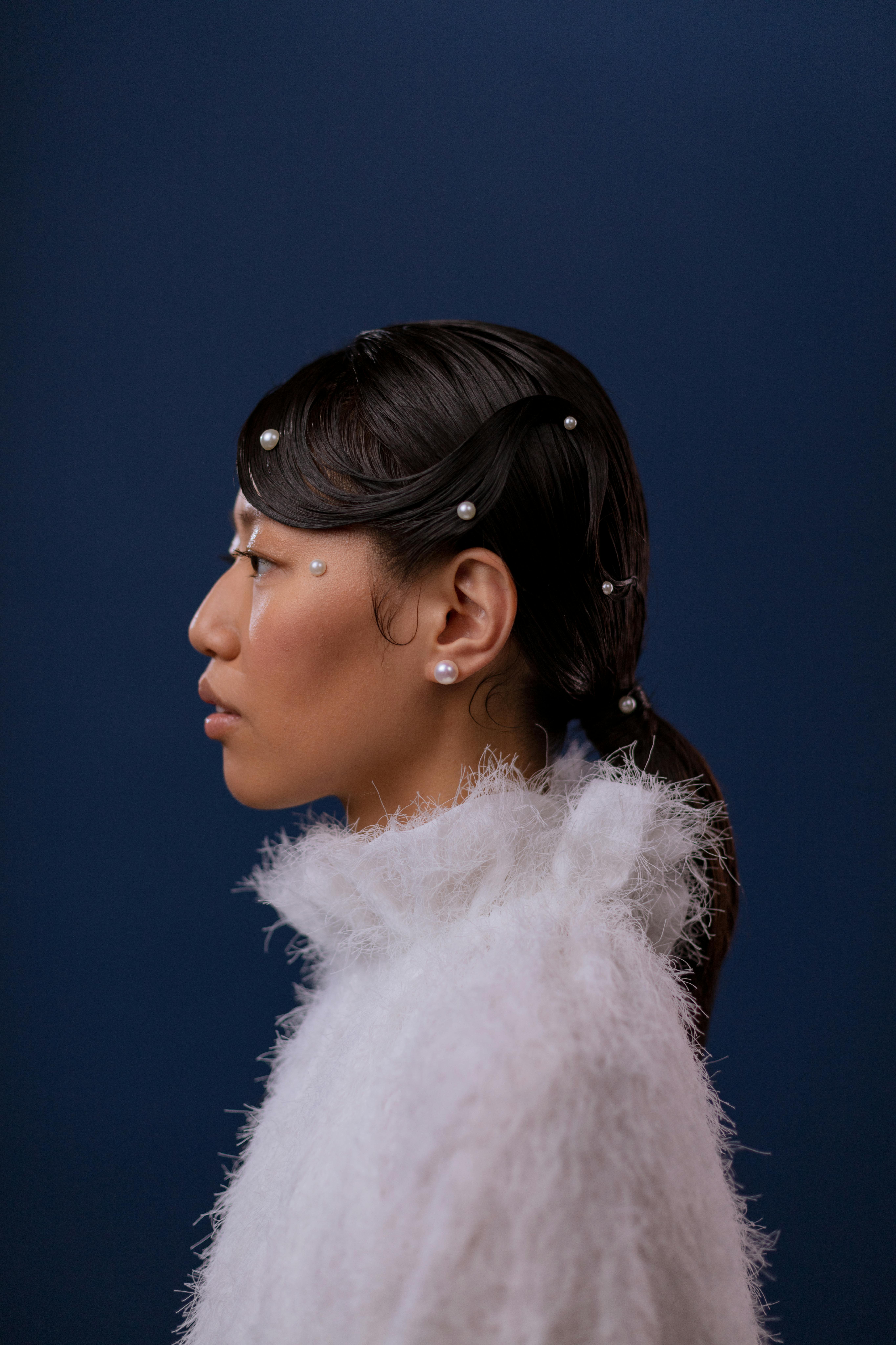 Side profile of a woman with pearl accents and a white textured outfit against a blue background.