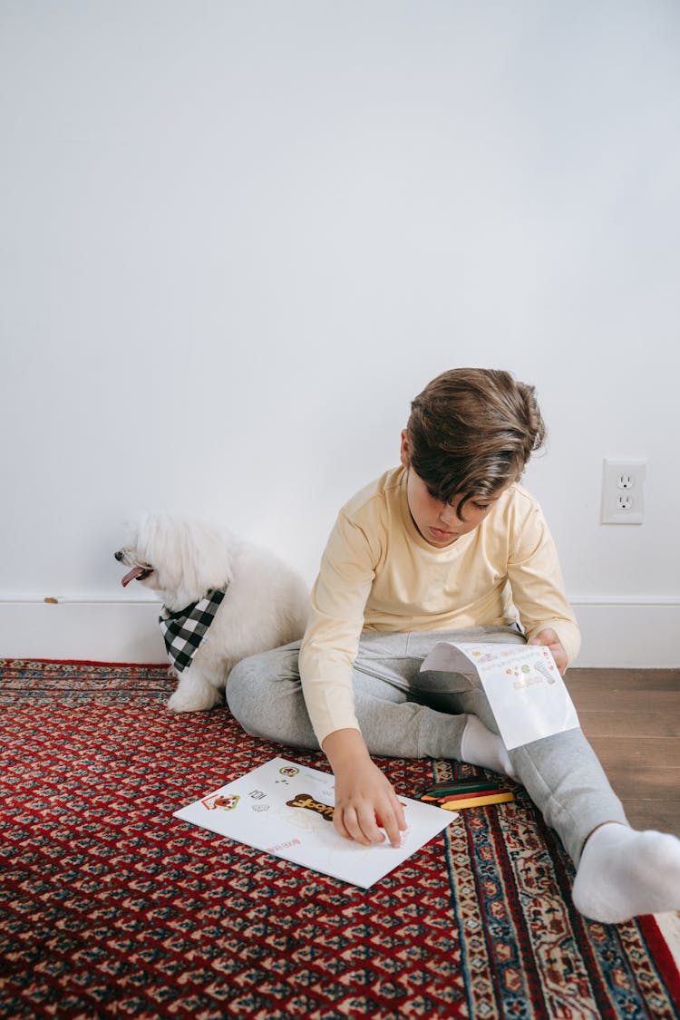 A Kid Putting Stickers On A Paper Near His Dog