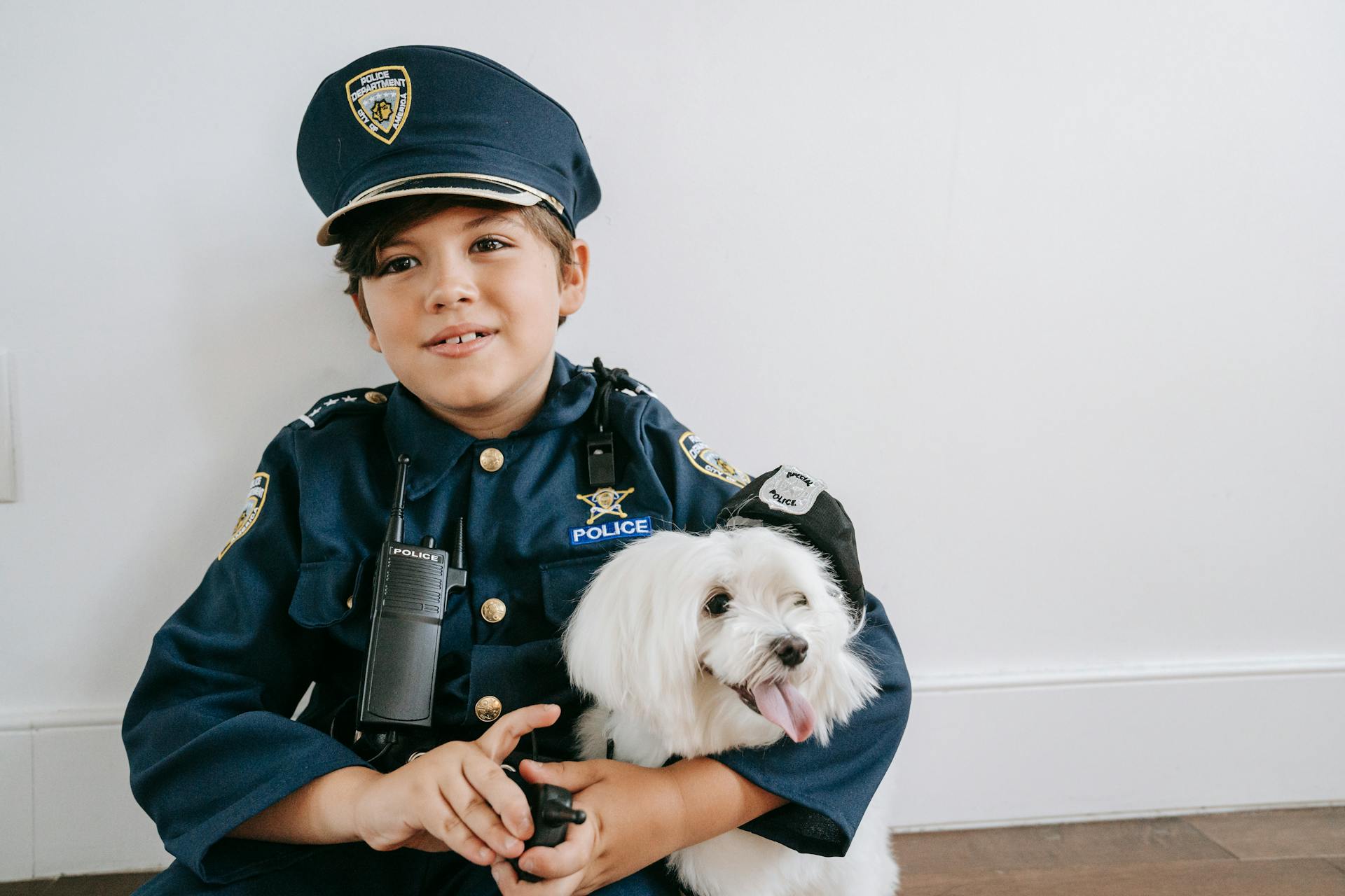 Photo of a Boy in a Police Costume Sitting Beside a White Dog