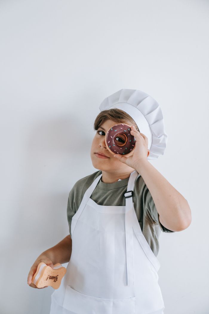 Child in a chef hat proudly holding a glazed donut