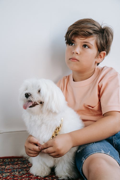 Photo of a Boy in a Salmon Shirt Sitting with His White Dog