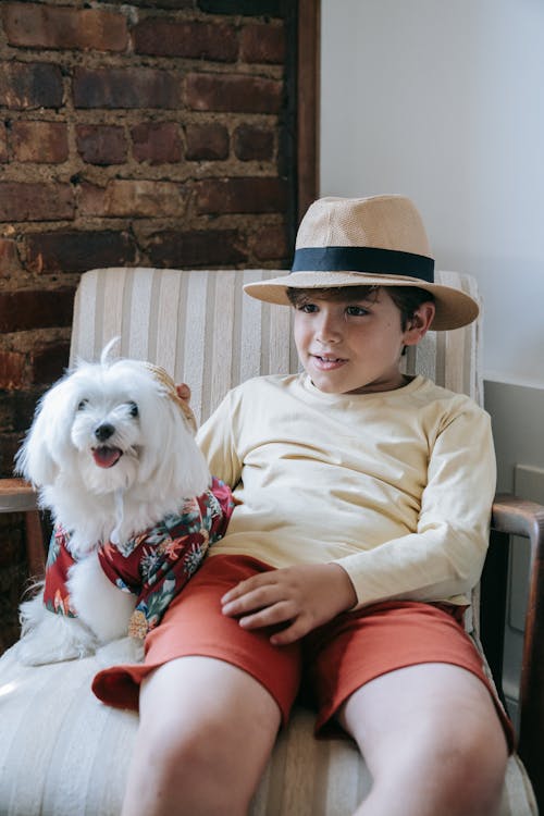 Photo of a Boy in a Hat Sitting Beside a White Dog