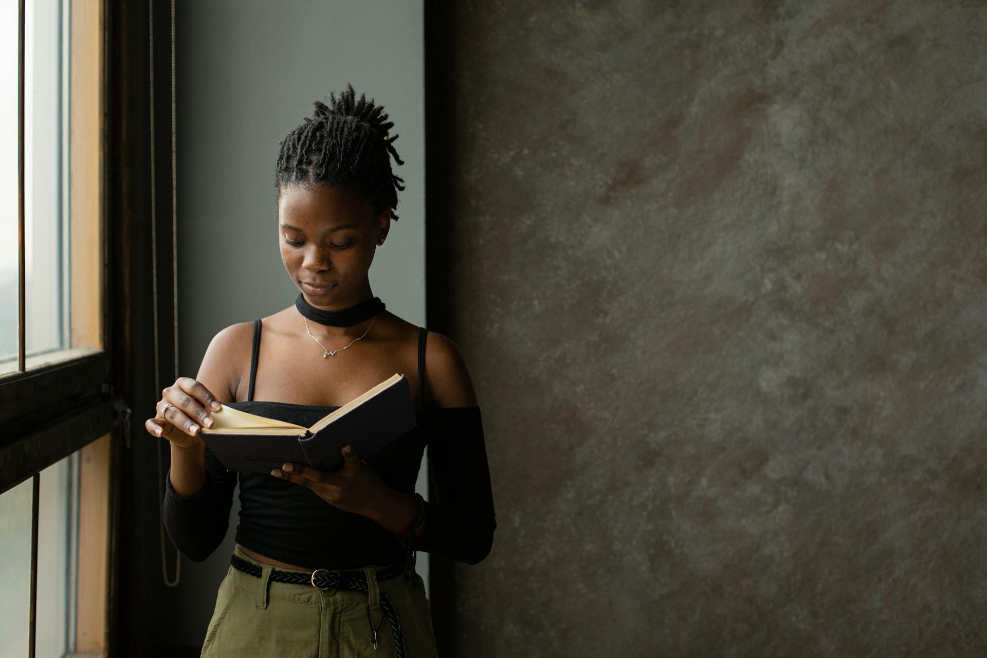 Focused young black woman reading book in light room