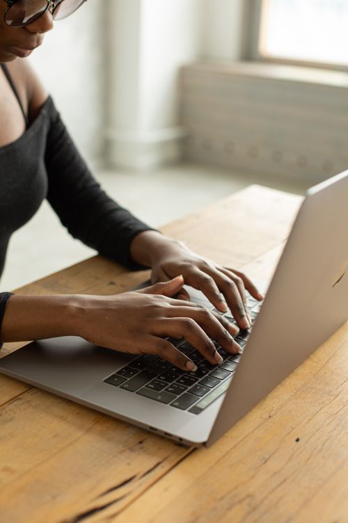 Free From above of crop unrecognizable African American female freelancer in eyeglasses sitting at table with opened netbook and typing on keyboard in light modern apartment Stock Photo
