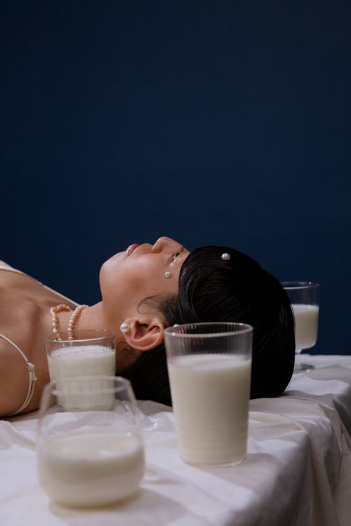 Free A woman with pearls and glasses of milk on a white sheet, set against a blue backdrop. Stock Photo