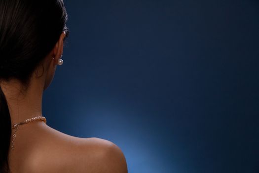 Close-up of a woman's bare shoulder adorned with pearl jewelry against a blue background.