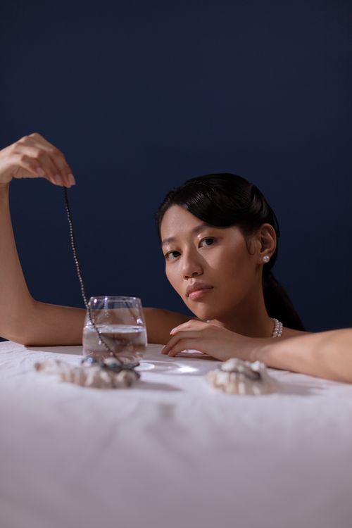 Free A woman with jewelry reflecting in water against a deep blue backdrop, exuding elegance and mystery. Stock Photo
