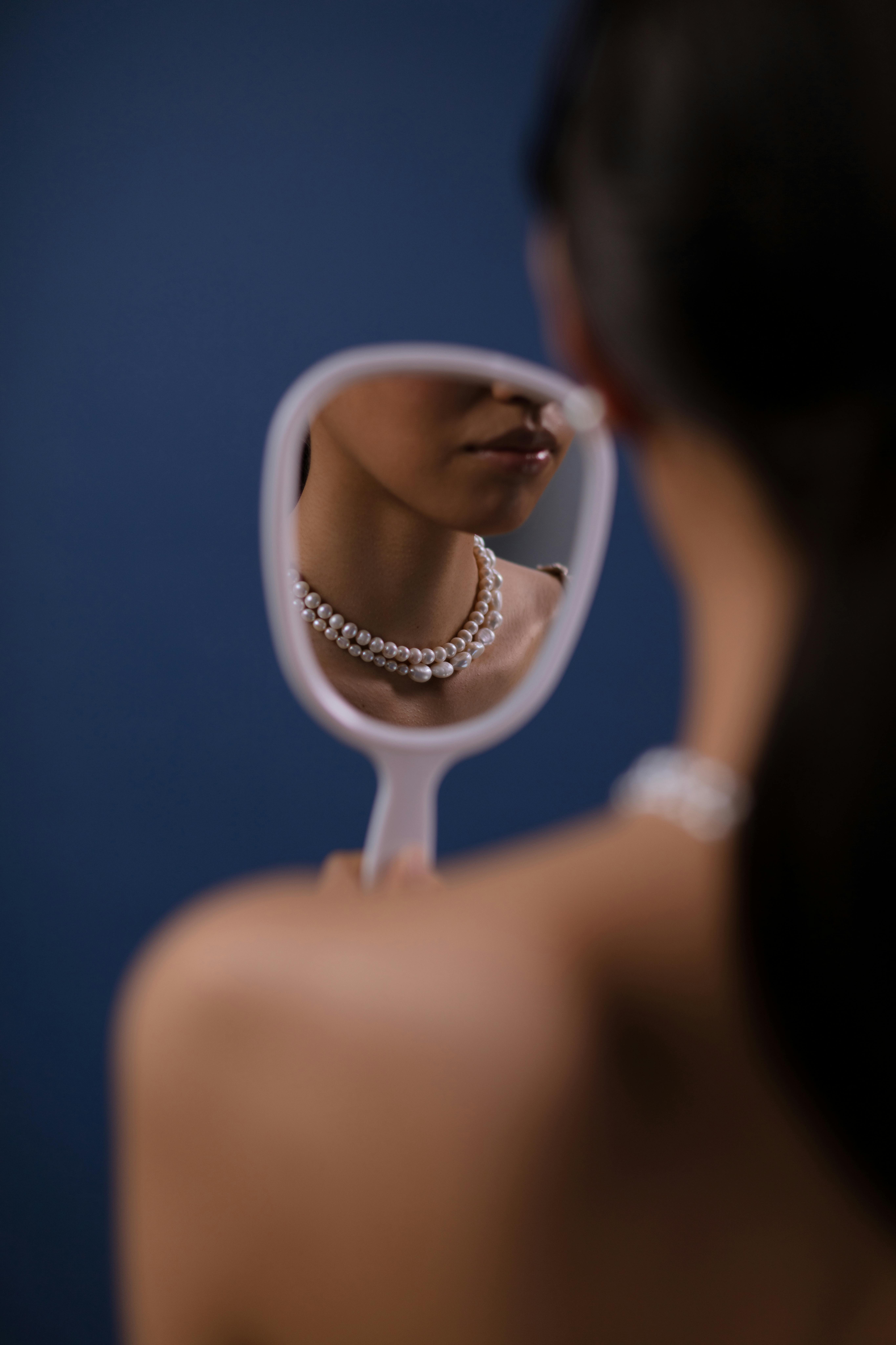 A woman's elegant pearl necklace is perfectly captured in a mirror's reflection.