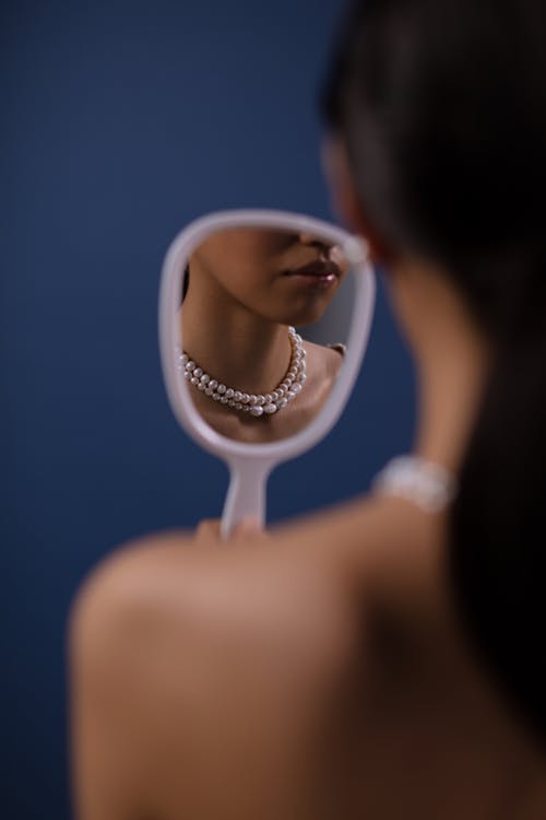 Free Woman's Reflection in the Mirror while Wearing Her Pearl Necklace Stock Photo