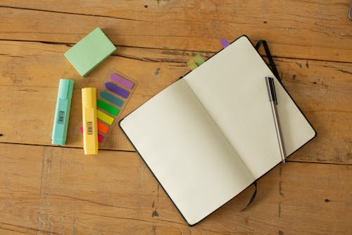 Free Top view of opened sketchbook with blank pages and pen with coloured markers and bookmarks arranged on wooden desk Stock Photo