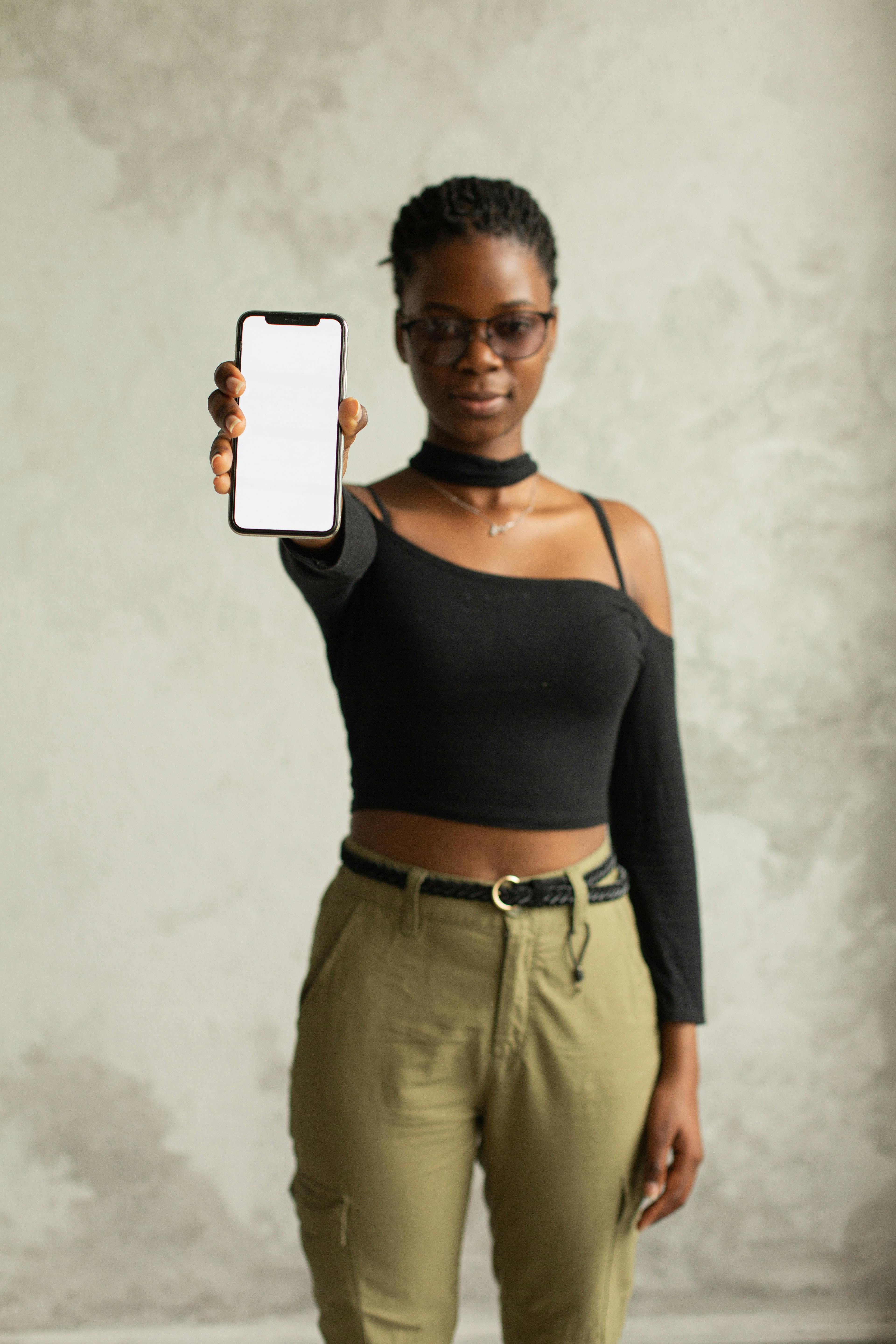 emotionless black woman standing with mobile with blank screen