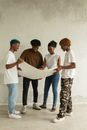 Group of African American teenager standing near white wall and discussing project while working with paper