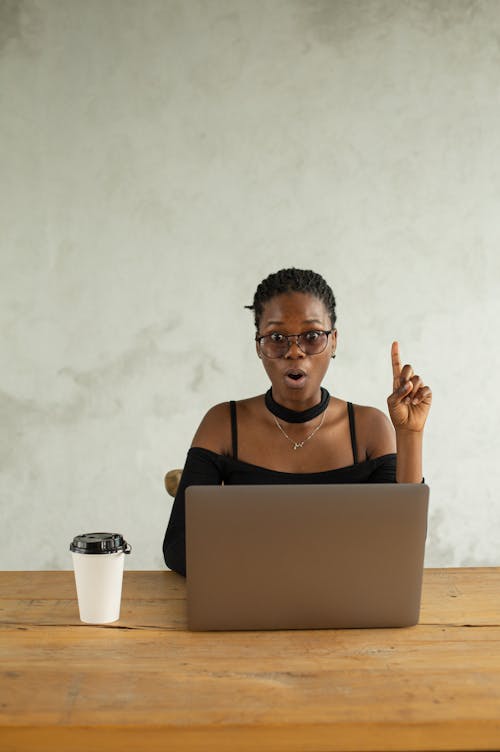 Free Young African American female entrepreneur sitting at table with netbook and takeaway coffee and looking enthusiastic about new ideas while looking at camera Stock Photo