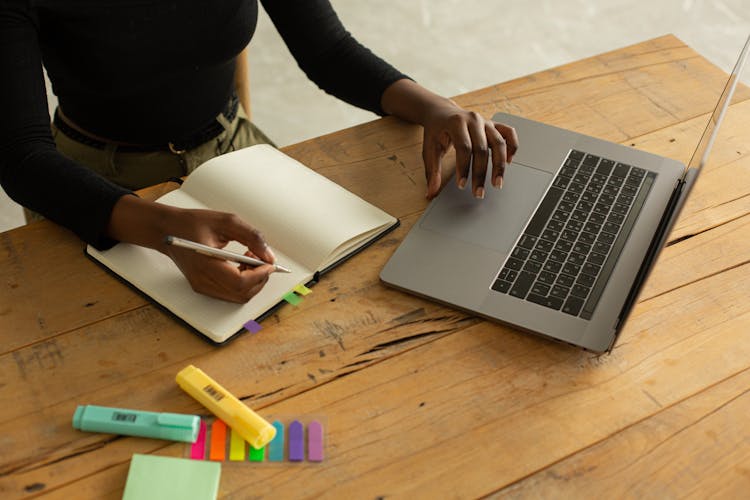 Crop Unrecognizable Black Woman Using Laptop And Writing Notes