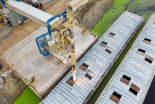 Aerial view of industrial barges and docking facility near green algae-infested water.