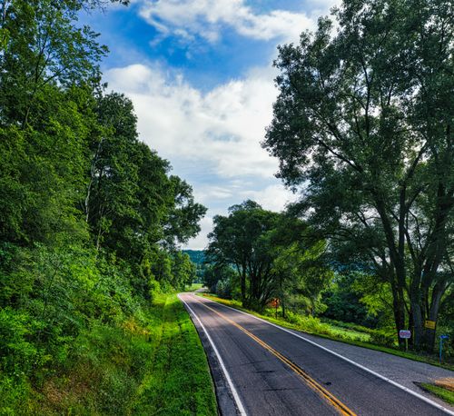 Free A picturesque road winding through green forests under a bright blue sky in Minnesota. Stock Photo