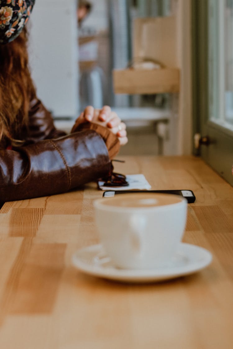 Photo Of A Woman Sitting In A Cafe With Cup Of Coffee In Foreground