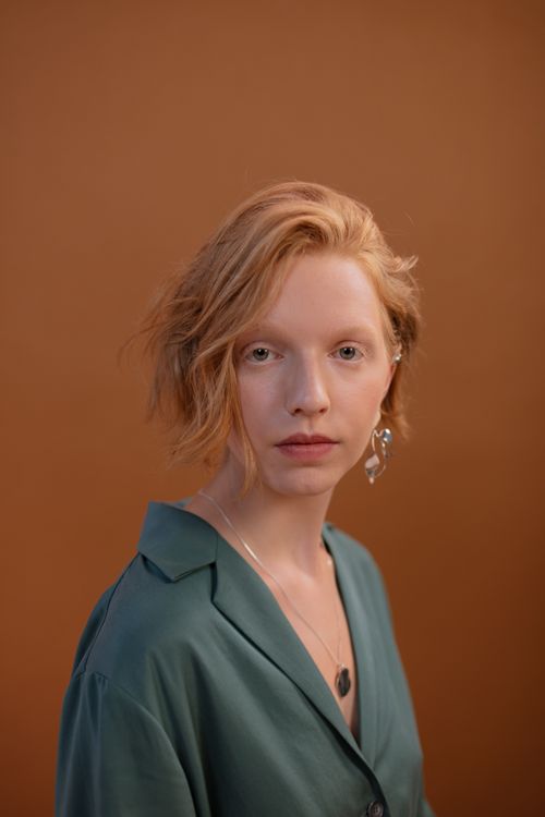 Free Elegant portrait of a woman with red hair and unique earrings against a neutral background. Stock Photo