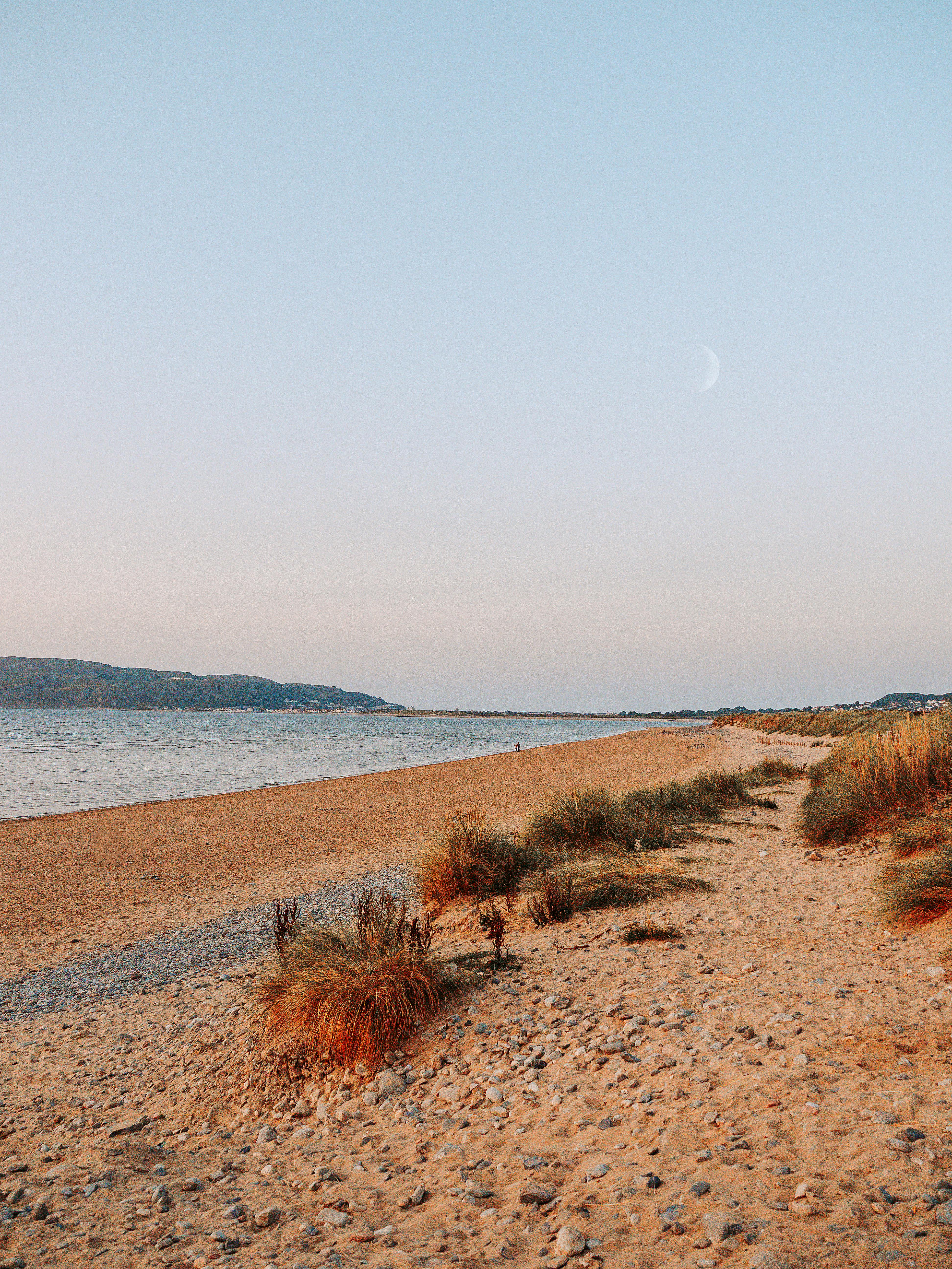 Peaceful beach scene at sunset with a crescent moon in the sky.