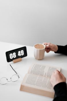 A peaceful morning scene with coffee, a book, and a smartphone displaying the time, offering cozy vibes.