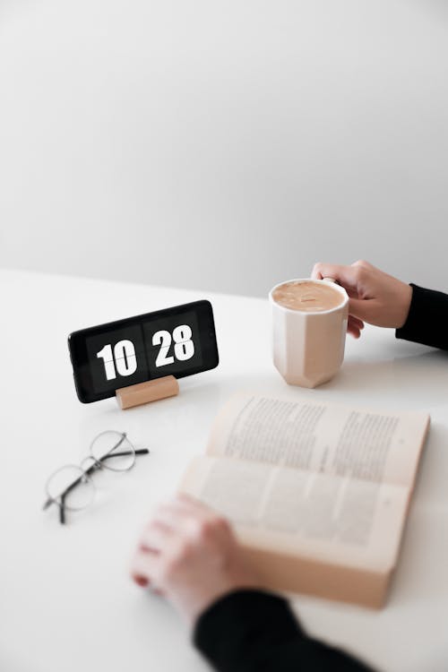 Free Person Reading a Book with Digital Clock on a Desk Stock Photo