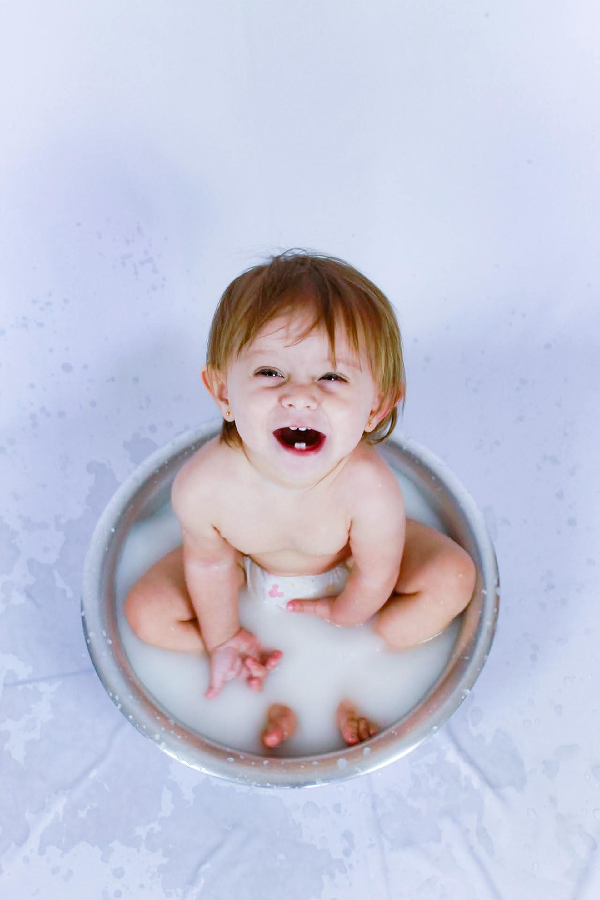 Happy baby taking a milk bath, smiling joyfully in a round tub.