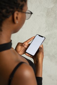 Back view of woman holding smartphone with blank screen, ideal for app mockups or design presentations.